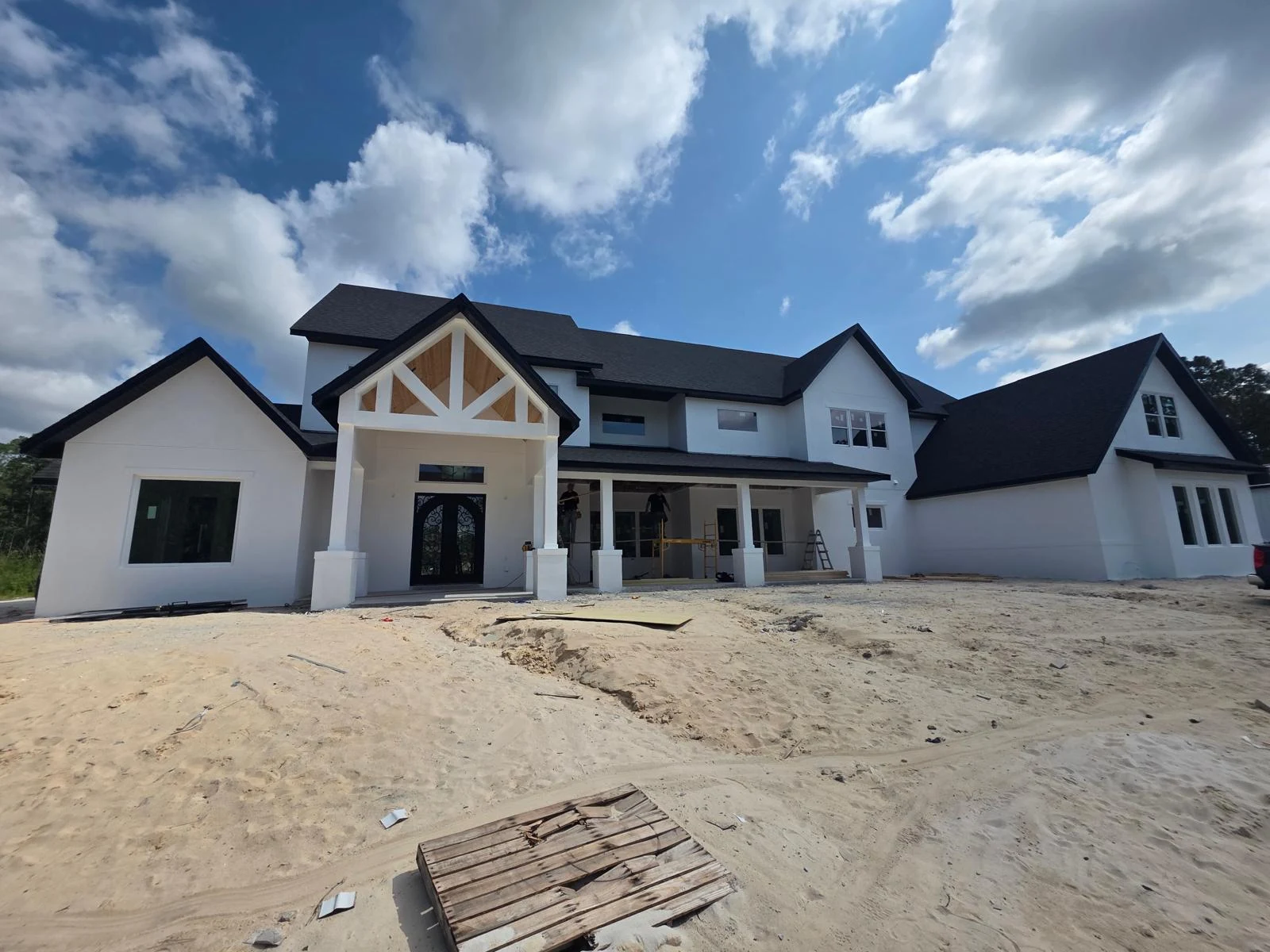Custom home exterior with crew on site under a dramatic sky