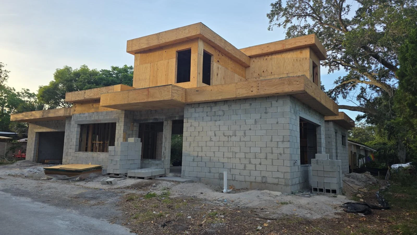 Custom home exterior mid-construction at golden hour, block walls with wood roof structure