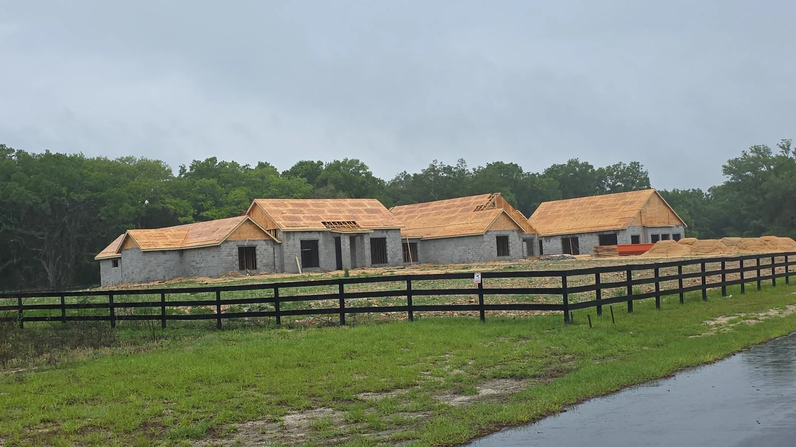 Custom home with wood shake roof nearing completion, next to a rural pasture fence
